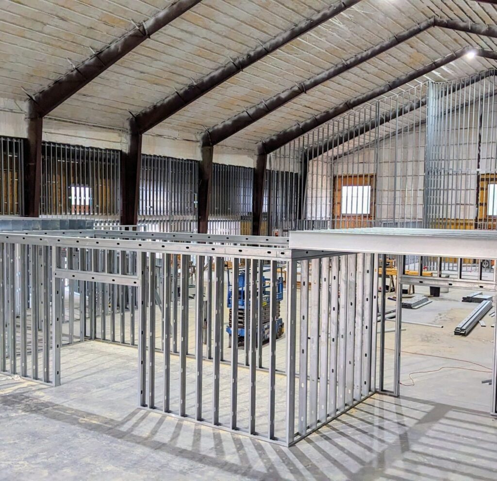 Framing construction in a spacious industrial setting, showcasing metal studs and framework for drywall installation, highlighting craftsmanship by Framing to Drywall.