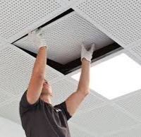 Worker installing an acoustic ceiling panel in a commercial space, showcasing professional craftsmanship relevant to Framing to Drywall's services.