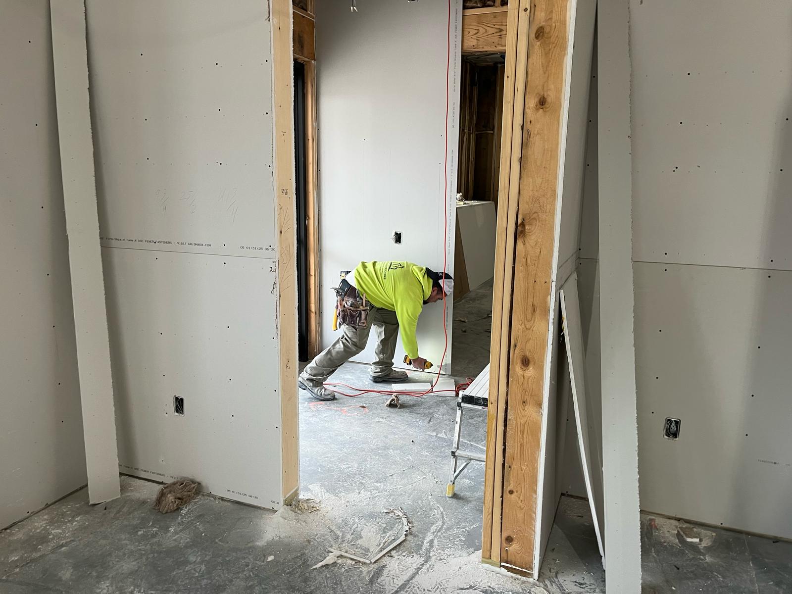 Construction worker measuring drywall in a basement framing project, showcasing craftsmanship in framing and drywall installation.