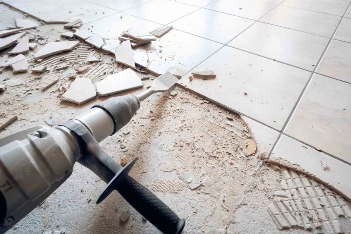 Tile demolition process with a power tool, showcasing broken tiles and debris on the floor, illustrating construction and renovation work by Framing to Drywall.