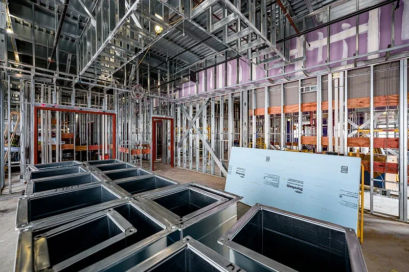 Construction site interior with metal framing, drywall sections, and storage containers, illustrating framing techniques relevant to commercial projects.
